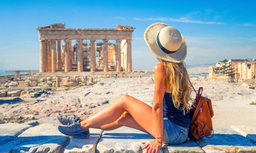 Young female tourist with a brown bag looking at Parthenon Athens Greece temple.